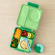 Green bento box with compartments filled with fruits and a fork on a beige surface