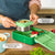 Green lunch box with compartments and a thermos for hot food, on a wooden table.