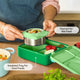 Green lunch box with compartments and a thermos for hot food, on a wooden table.