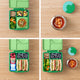 Green bento box with compartments filled with various food items on a wooden surface.