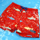 Red swim shorts with shark pattern on a blue water background