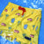 Yellow swim shorts with beach-themed pattern on a blue background