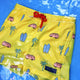 Yellow swim shorts with beach-themed pattern on a blue background