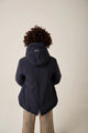 Person wearing a dark blue hooded jacket on a beige background