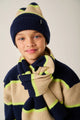 Child wearing a navy and beige striped sweater, navy hat, and matching scarf with green accents.